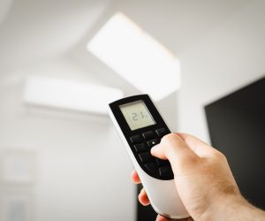 Ruka drži daljinski upravljač i podešava temperaturu klima uređaja radi manje potrošnje struje